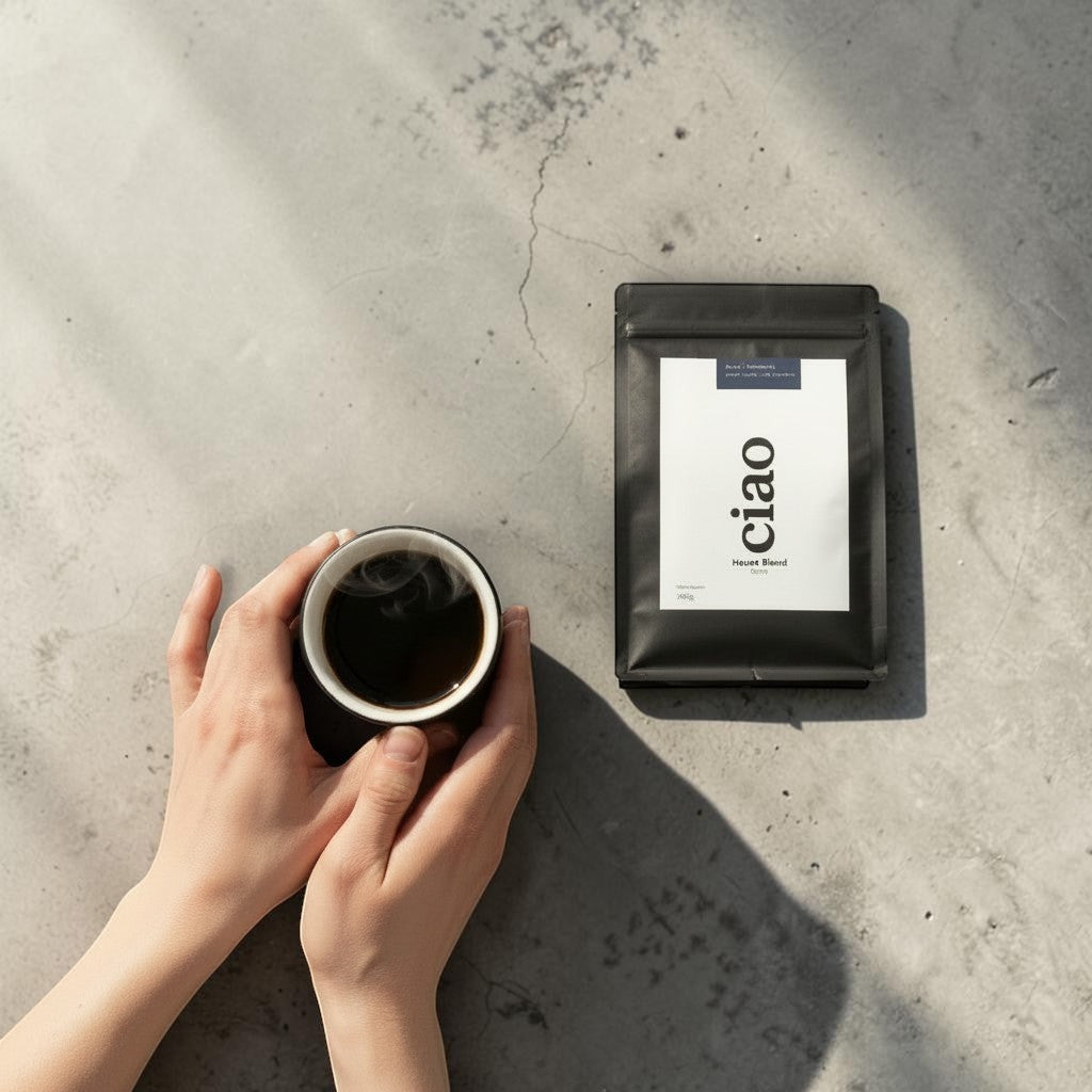 Say Ciao Coffee House Blend coffee bag next to a steaming cup of black coffee held by hands. Medium roast.